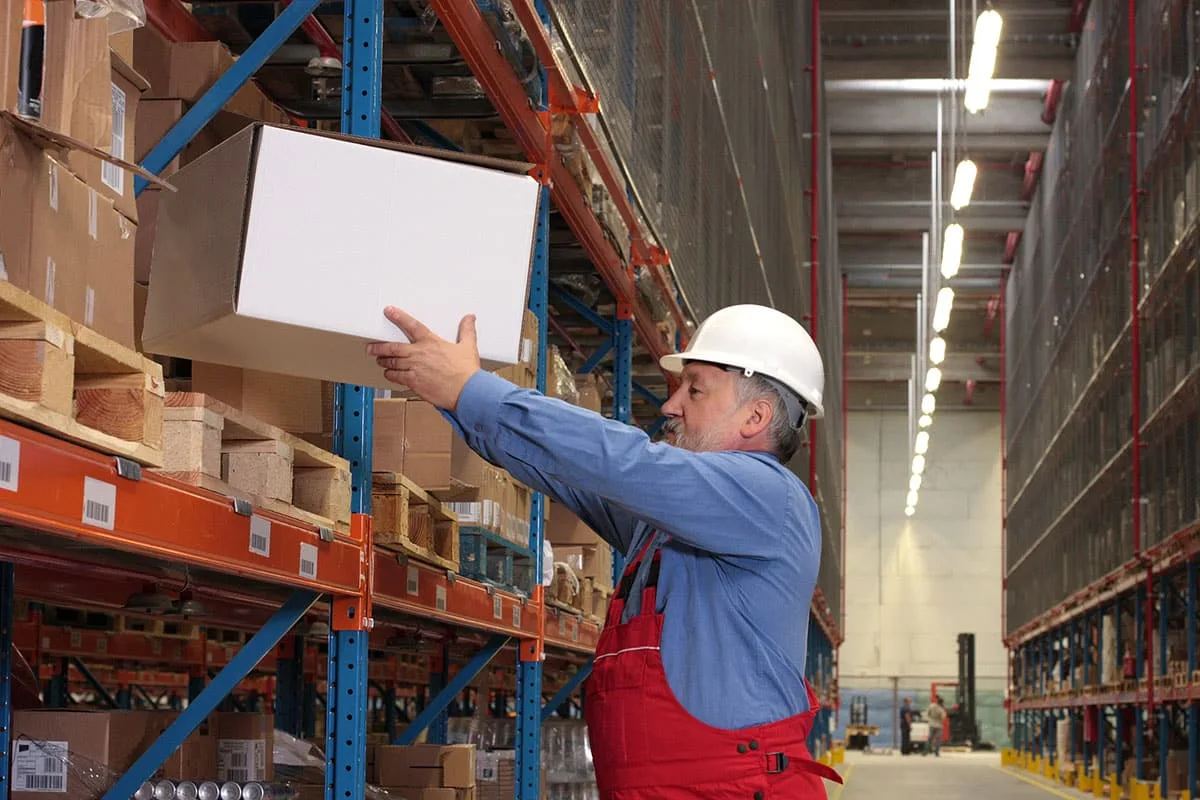 senior worker in uniform putting box on shelves in warehouse
