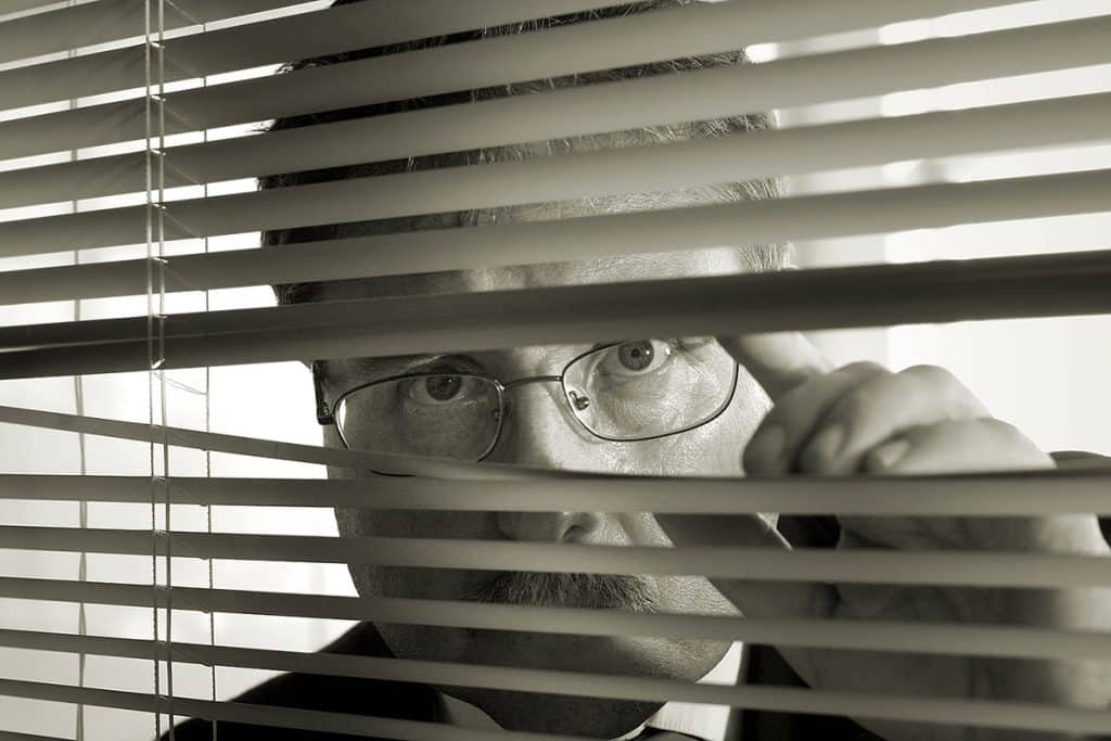sepia picture of a man peeking through blinds